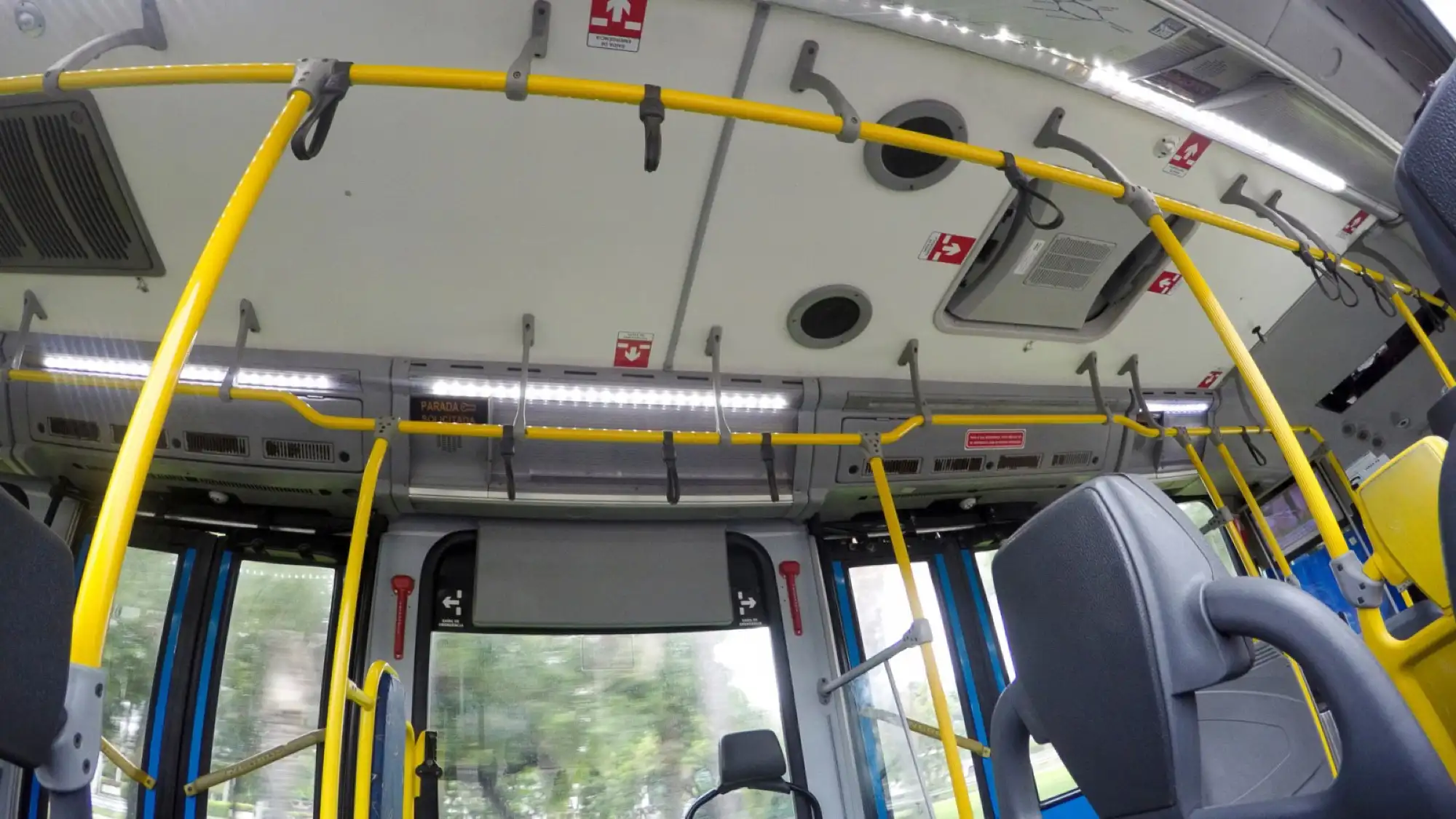 Interior of a BRT bus in Rio de Janeiro, showing yellow handrails, hanging straps, and seats with a view through the windows.