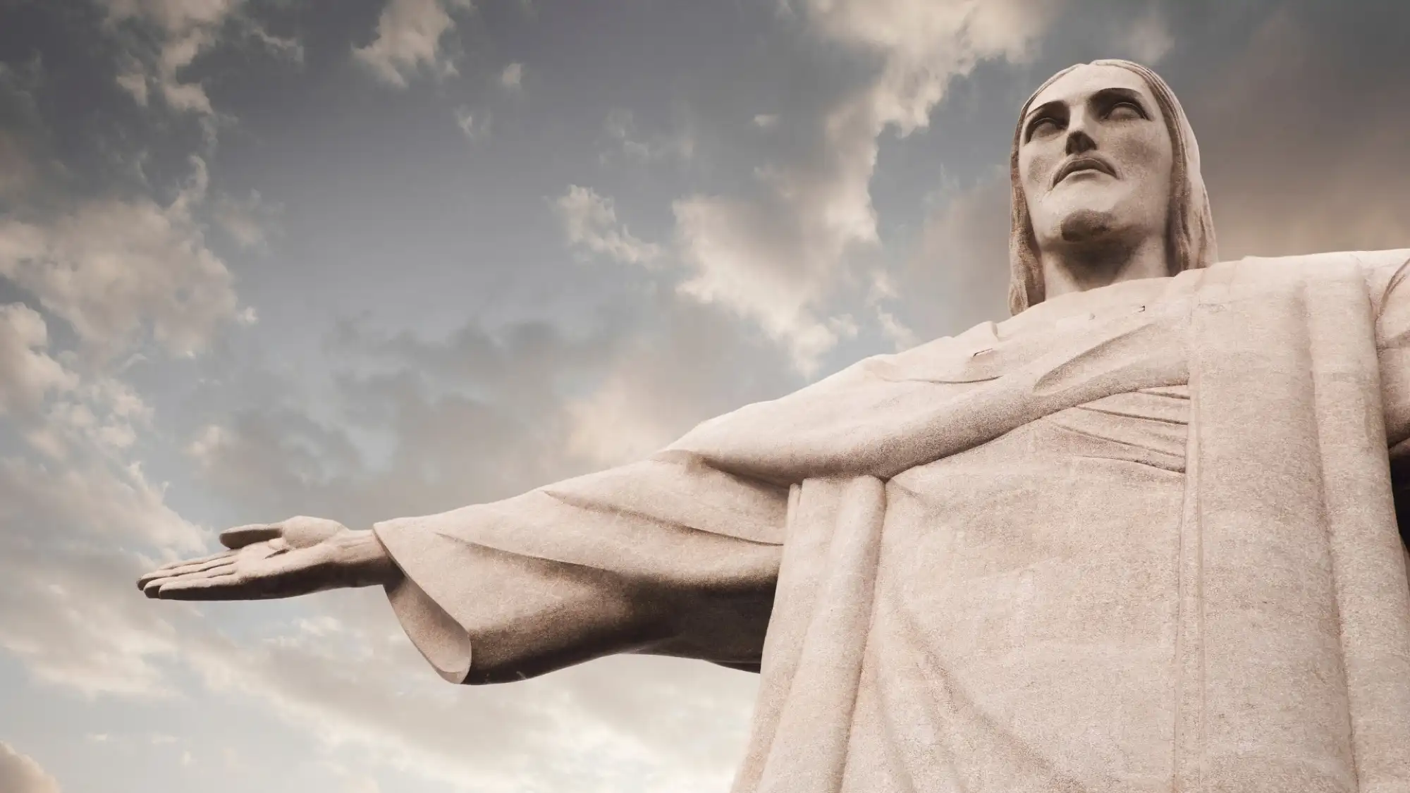 Close view of the head, shoulder and outstretched arm of Christ the Redeemer against a cloudy sky, the mosaic surface visible