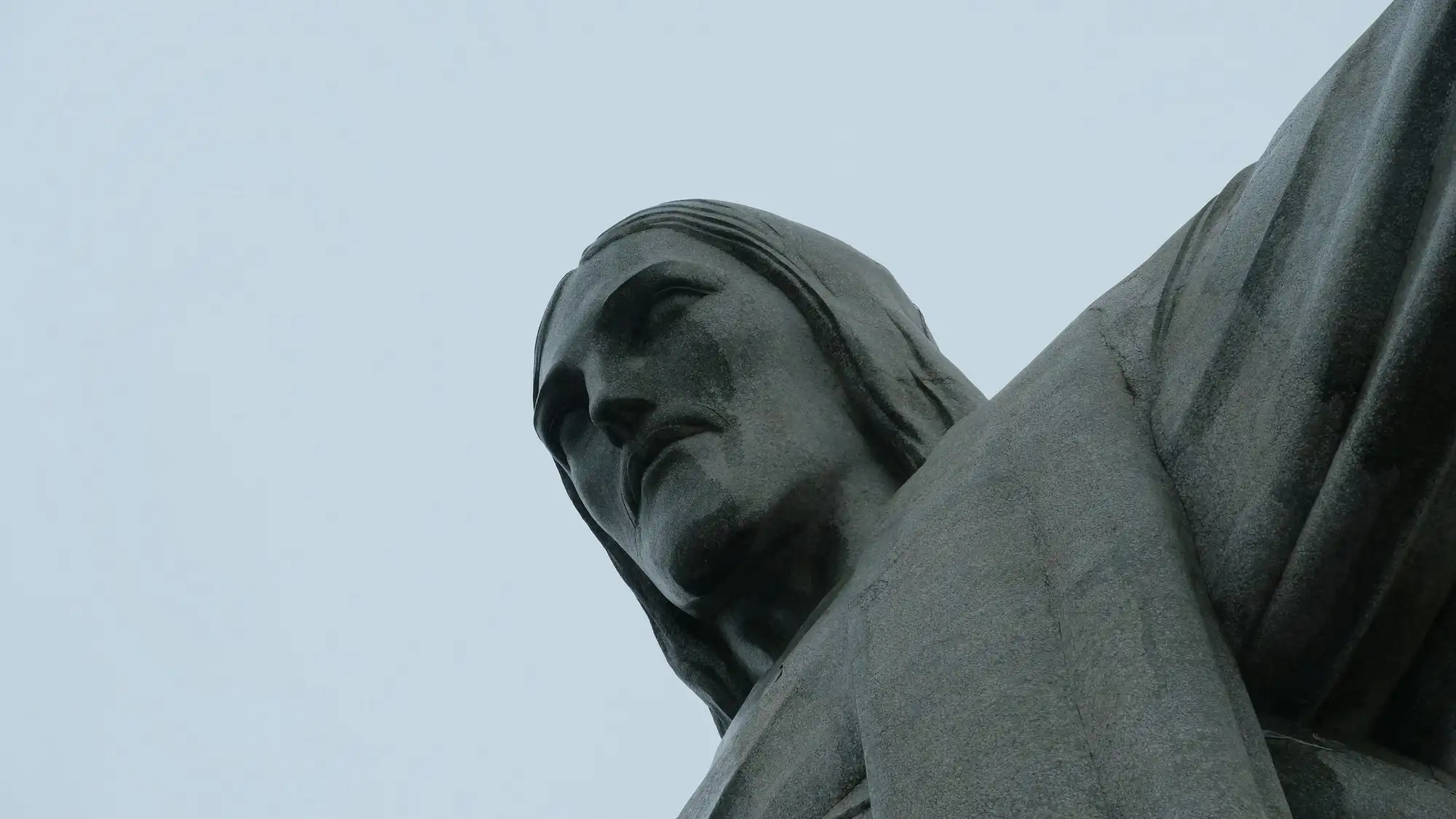 La tête et l’épaule du Christ Rédempteur vues d’en bas, le gris patiné de la stéatite sur un ciel pâle
