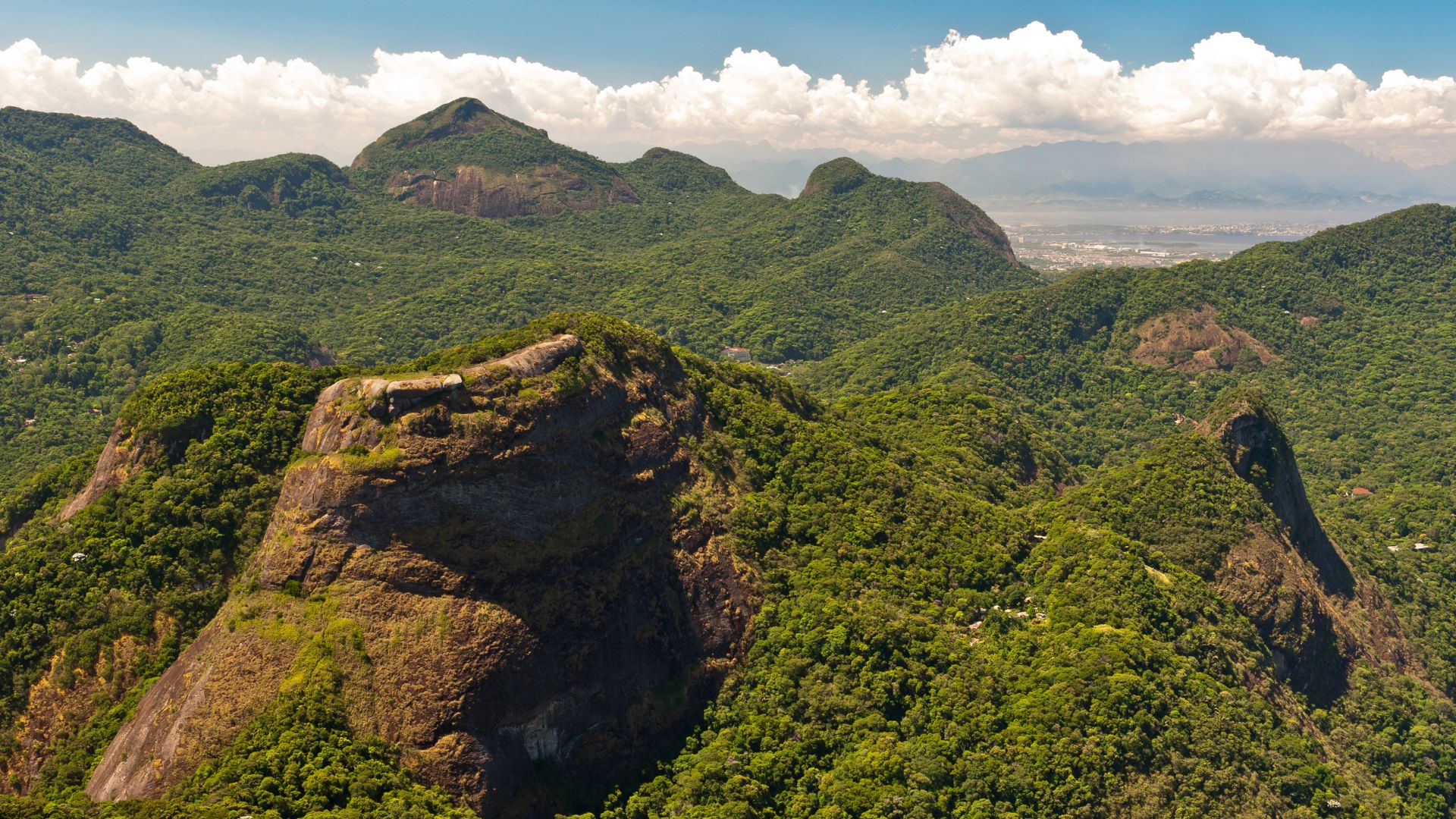 Expansive view of the mountain ranges covered in dense green forest in Tijuca National Park, with layers of peaks extending towards the horizon.