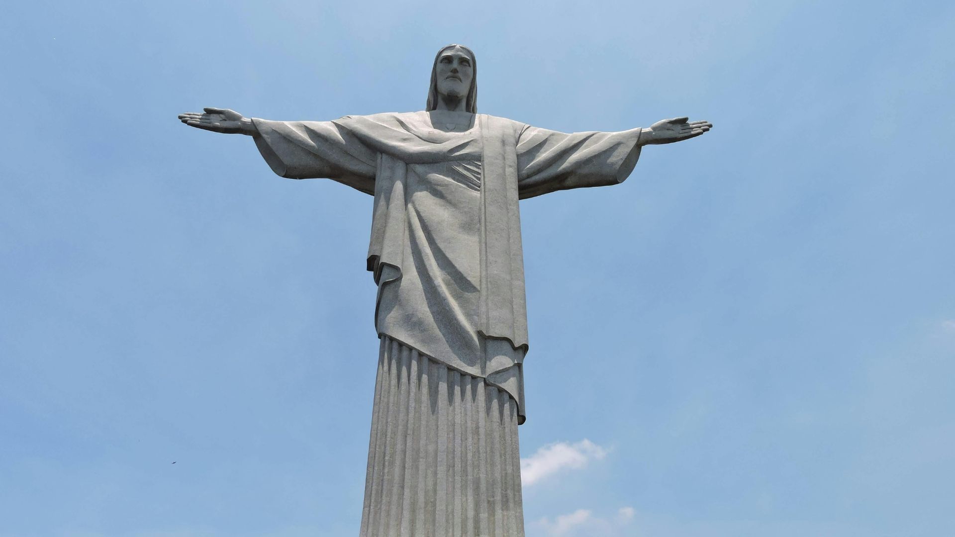 Close-up of the Christ the Redeemer statue in Rio de Janeiro, showing the statue's outstretched arms against a clear blue sky.